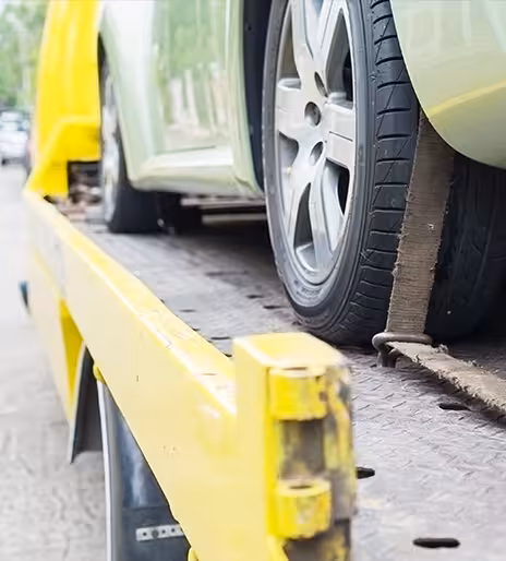 A green car strapped to the back of a yellow tow truck.